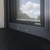 Profesjonalny montaż parapetów zewnętrznych. Ciemny parapet i szara rama okna z moskitierą.