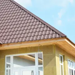 Okap dachu dwuspadowego z brązowej blachodachówki, widoczny fragment ocieplonej ściany i okien.