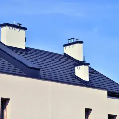 Nowy dom z ciemnym dachem i białymi kominami. Widać nowoczesne rynny bezokapowe, które dyskretnie odprowadzają wodę.