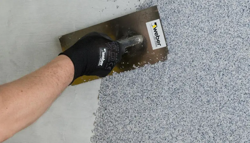 Nakładanie tynku mozaikowego na ścianę za pomocą kielni.