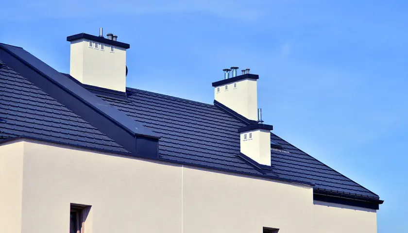 Nowy dom z ciemnym dachem i białymi kominami. Widać nowoczesne rynny bezokapowe, które dyskretnie odprowadzają wodę.